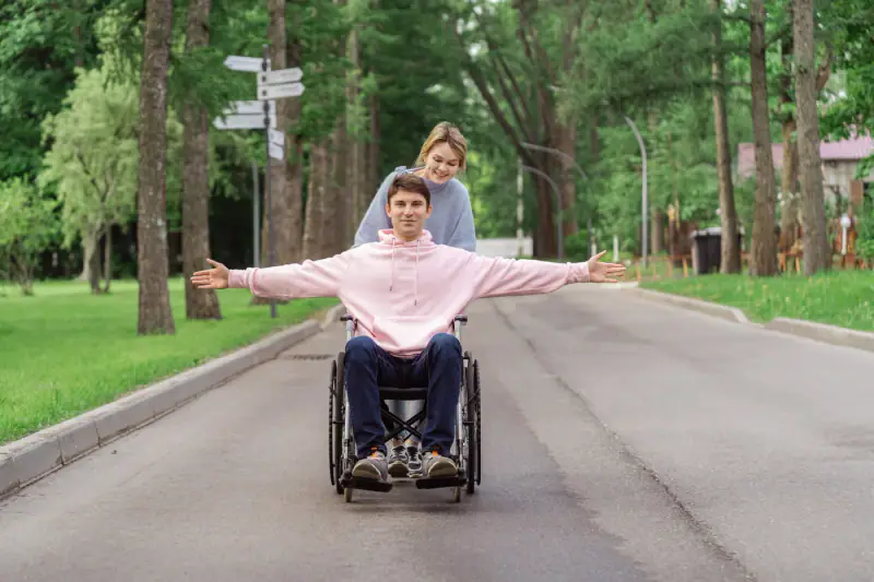 A smiling wheelchair user enjoying time outdoors with a support person.