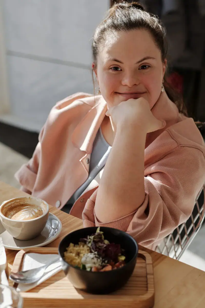 A smiling woman with Down syndrome enjoying breakfast at a table.