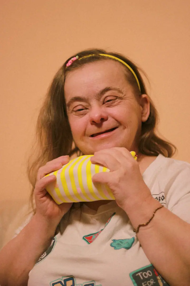 A smiling woman with Down syndrome holding a wrapped gift.