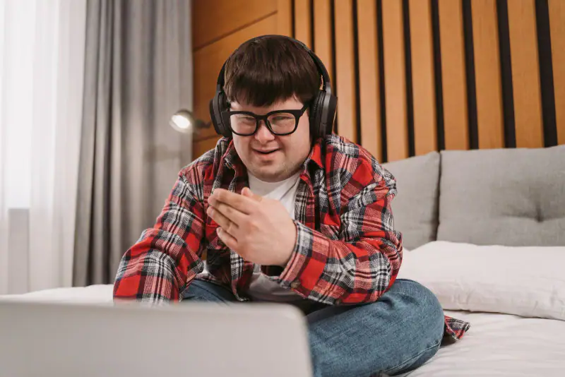 A smiling man with Down syndrome using a laptop and headphones.