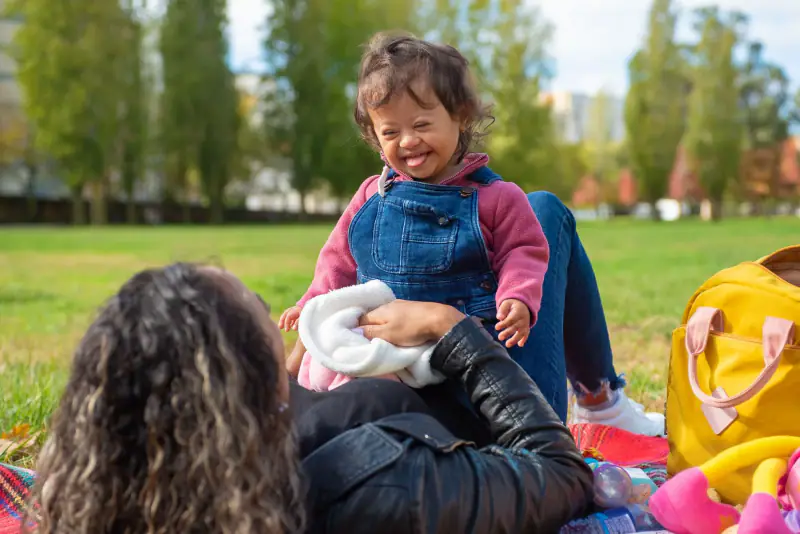 A smiling young child with Down syndrome enjoying a picnic in a sunny park.
