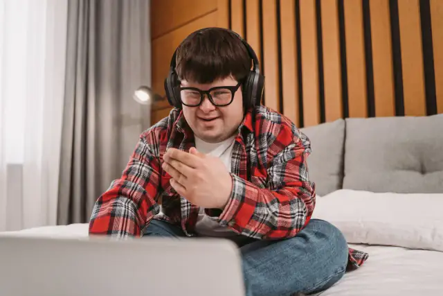 A smiling man with Down syndrome using a laptop and headphones.