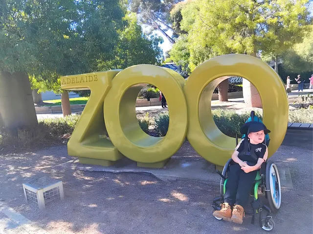 A child using a wheelchair beside the large Adelaide Zoo sign.