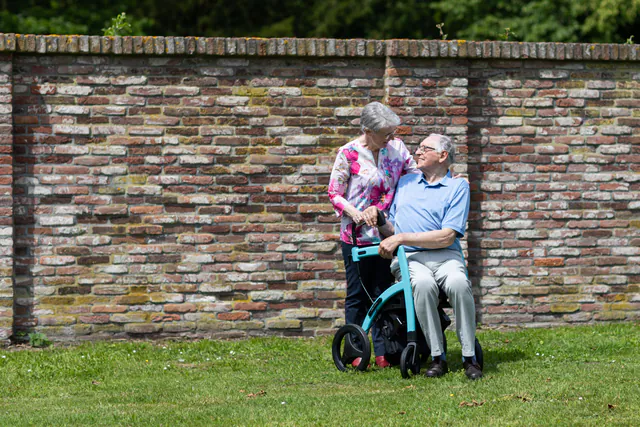 An older couple spending time together outdoors, with a mobility aid beside them.