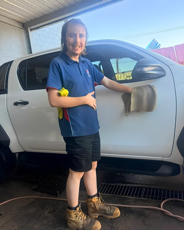A smiling man holding a cleaning cloth beside a white vehicle.