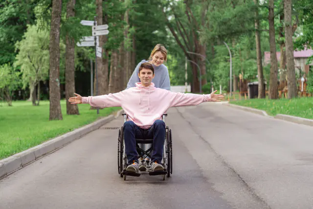 A smiling wheelchair user enjoying time outdoors with a support person.