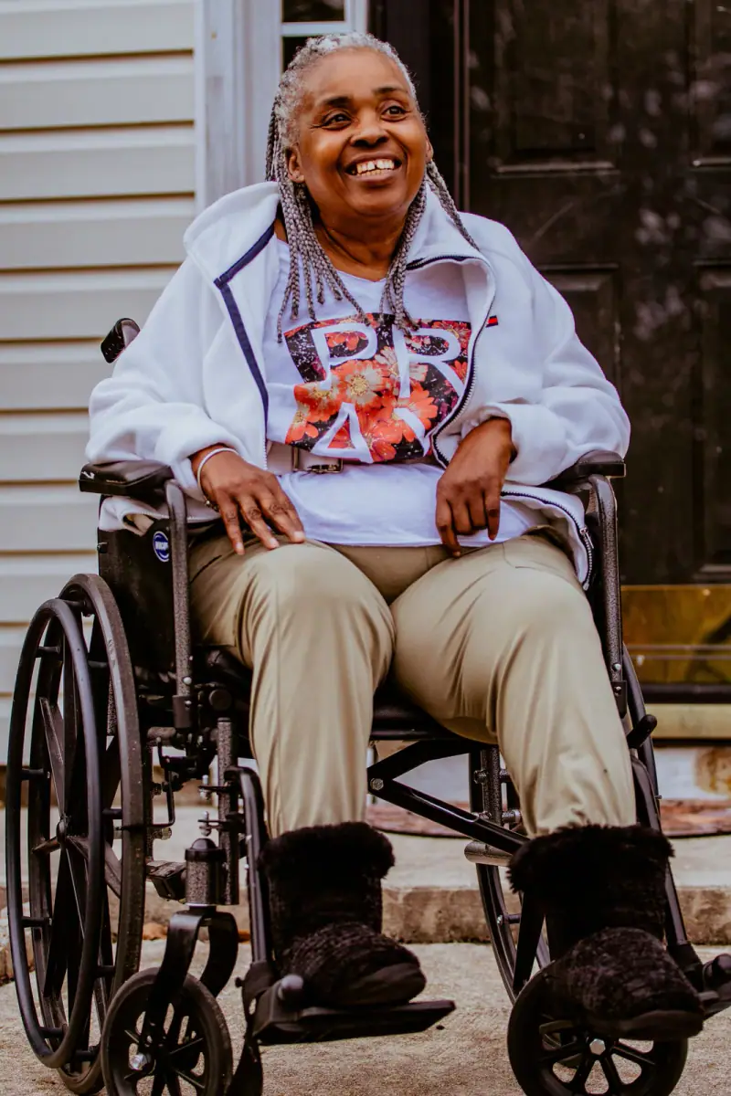 A smiling older woman sitting in her wheelchair outdoors.
